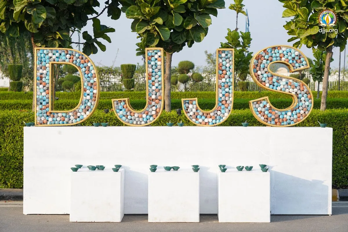 Large letters spelling DJJS, decorated for Diwali, standing in a garden at Nurmahal Ashram